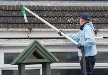 A window and gutter cleaner cleaning Dirty clogged white plastic pvc gutters and drain pipes with...