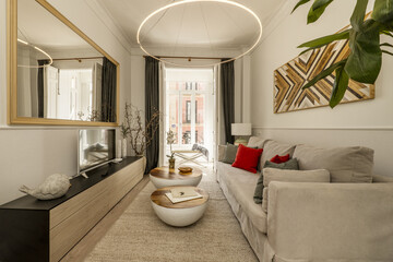 Living room of a vacation rental house with a wooden sideboard with drawers, a large mirror and a beige fabric sofa and a large window with a view