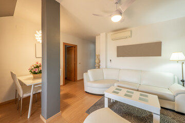 Living room of a house with a white leather sofa covering one wall and a dining table and a matching coffee table