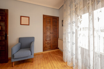 Corner of a bedroom with natural wood flooring, a built-in wardrobe with paneled doors and a blue fabric single armchair