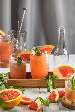 Grapefruit Cocktail in highball glasses or mocktails surrounded by ingredients and bar tools on light gray table surface