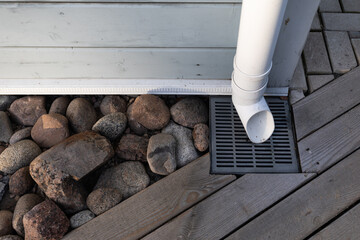 A white rainwater drain pipe and a drainage system with a grate built into the wooden platform and decorated with stones