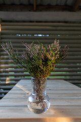Vase with a bouquet of flowering cut heather on the table in the village house