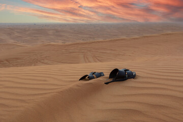 Lost in the desert. A pair of sandals covered by sand. Beautiful sunset sky