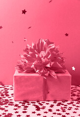 Gift box and falling confetti in trending Color of the Year 2023. Viva Magenta. Copy space for your design. Vertical photo. The concept of a holiday, invitations, sales, invitations to birthday