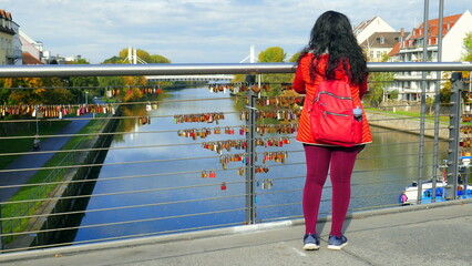 junge Frau mit schwarzen Haaren schaut in Bamberg über Brücke der Regnitz mit vielen...