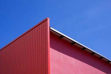 Fototapeta premium Low angle view of empty red corrugated steel wall decoration on pink wall of modern building against blue clear sky background