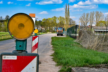 Baustelle mit rot-weißer Warnbarke mit gelben Blinklicht als Absperrung und Baustellen-LKW im...