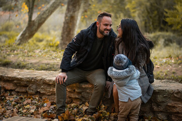 familia sonriendo y jugando con las hojas caidas del otoño en el bosque