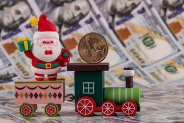 Figurine of Santa Claus and a wooden train against the background of American dollars