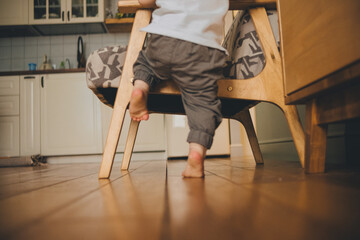 Bare heels of a toddler standing next to an armchair on a wooden floor at home