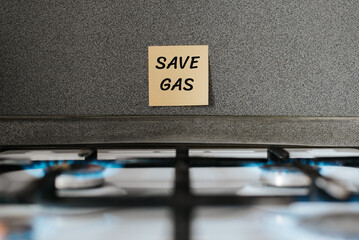 Gas saving concept Responsible household energy consumption. Inscription on sticker Save Gas on kitchen wall above gas stove with burning burners