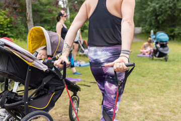 Backside photo taken from a woman pulling elastics with her baby next to her, in group session with other mothers outside on a grass field
