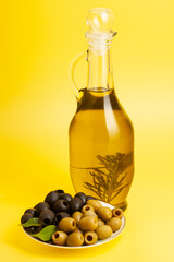 Jug with olive oil, green and black olives on yellow background.