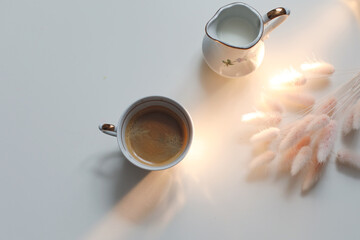 cup with coffee and milk jug on a white wooden background, closeup. Energy breakfast, morning routine concept