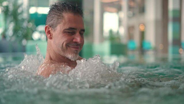 Wellness spa - older white man in his 50s relaxing enjoying hydromassage in pool. Leisure and lifestyle, real authentic footage.