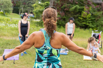 Obraz premium Backside photo taken of an instructor giving instructions outside on a grass field to mothers with their children working on their health