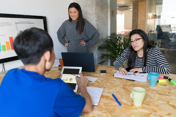 Office table with three Asian people sitting and using devices while working with graphics.