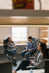 Group of three young Chinese people sitting in chairs in office and talking.