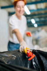 Vertical selective focus shot of blurred female worker in latex gloves sorting diverse waste for...
