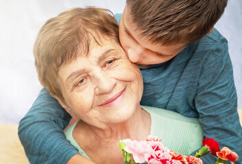 Boy giving a bunch of flowers to grandmother. Grandson and grandma spending time together.  Kindness to senior (elderly) woman. Happy Mother's Day, grandmother day, International Women's Day. - obrazy, fototapety, plakaty
