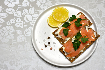 crisp bread slices with salmon slices, soft cheese, parsley and lemon slices on white plate