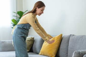 Household clean up, housekeeper asian young woman, girl cleaning, hand keeping put pillow on sofa, couch in living room at home. Messy maid or housewife organizing dirty and untidy. Chore concept.