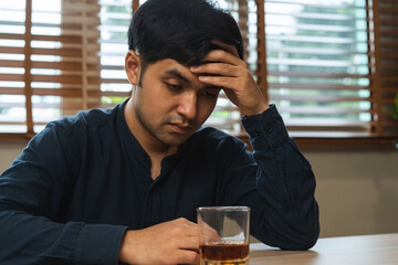 Alcoholism, hand cover face asian young man have headache, drink a glass of alcohol, whiskey expression stress, sitting alone at night. Treatment of alcohol addiction, suffer abuse problem alcoholism.
