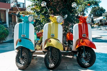 Gartenposter Scooter motorcycle on city street. Vintage classic retro scooters various bright colors on a sunny tourist street. Lifestyle, retro concept. © uladzimirzuyeu