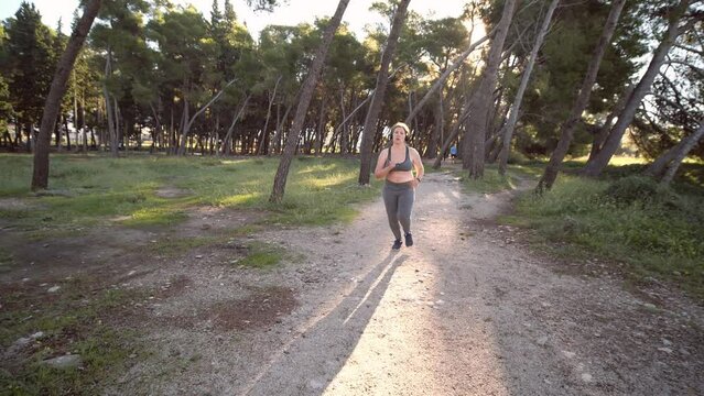 Bodypositive plus size female athlete jogging in the sunny park. Concept of weight loss and active lifestyle