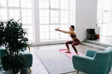 Slim woman doing yoga in chair pose at home
