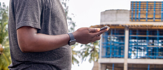 Young african man holding smartphone at construction site