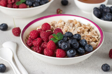 Oatmeal porridge with blueberries, raspberry and honey on light gray background. Breakfast meal concept, Close-up