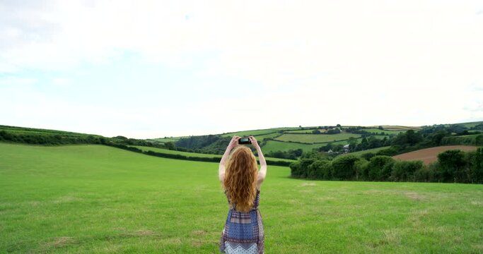 Woman photograph green landscape field with phone in Norway for travel, tourism or freedom on adventure, vacation and sightseeing in nature. Back view of tourist taking mobile pictures of environment