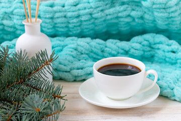 Cup of coffee, aroma reed diffuser, fir branch and a turquoise blanket