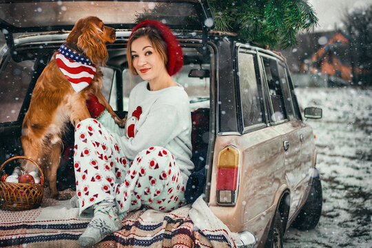 Christmas photo of a happy girl next to a retro car, a Christmas tree and an English Cocker Spaniel dog