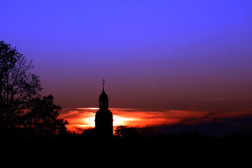Obraz premium silouhette eines barocken kirchturms und eines labbaums vor ienem leuchtenden himmel bei sonnenuntergang