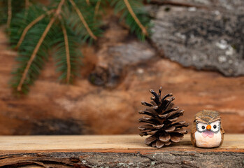 Pine cone and owl figurine on wooden desk with wooden background and green pine tree branches -...