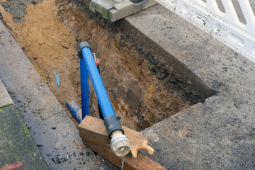 Konzept Baustelle, Erschließung und Versorgung: Blick von oben in eine offene Baugrube mit einem neuen Wasseranschluss mit Absperrventil, Rohren und anderen Versorgungsleitungen, selektiver Fokus