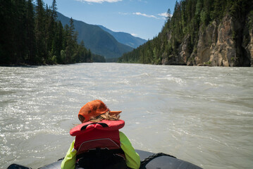 A child in life jacket sits on the bow of a raft in a wide river