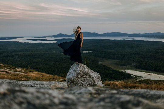 beautiful young woman and long dress balances on rock on mountaintop