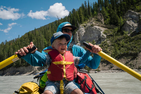 A father and son row a raft down a large river in the mountains