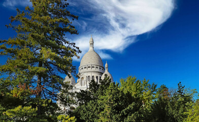 Beautiful view beyond green conifer trees on isolated dome of Sacre Coeur church, clear blue...