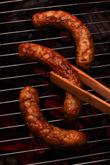 Juicy sausages sizzle on the grill, tongs ready to turn them over, capturing the essence of a perfect barbecue moment.