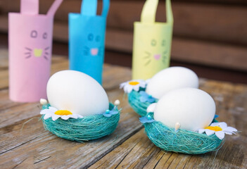 Easter eggs in nest with paper day hares on wooden table