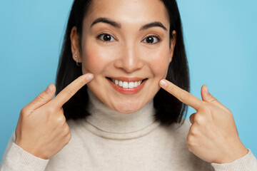 Portrait of pretty cheerful woman points index fingers at smile shows white teeth