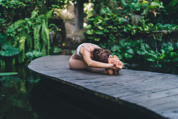 Faceless woman sitting on wooden bridge and doing yoga pose