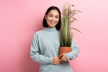 Cheerful housewife standing with pleased smile and holding flowerpot