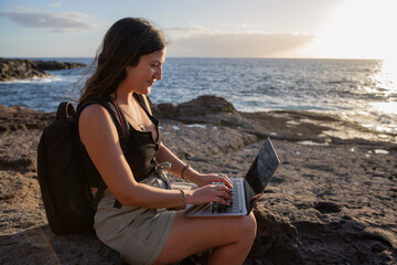 Girl using her computer at the sea, working remotely while travelling.