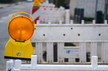 Konzept Baustelle: Nahaufnahme einer Baustellenlampe an einer rot-weißen Absperrung vor einer...